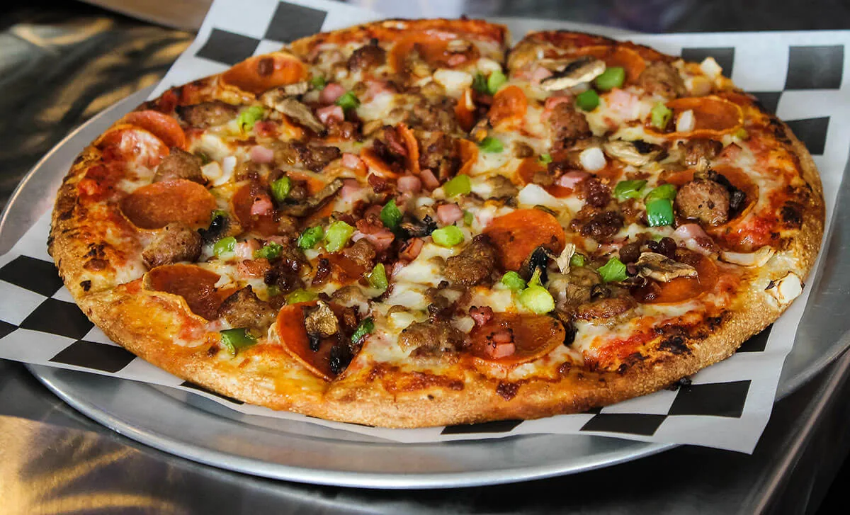 Big Jim's loaded pizza with peppers, meat, and melted cheese on a checkered tray